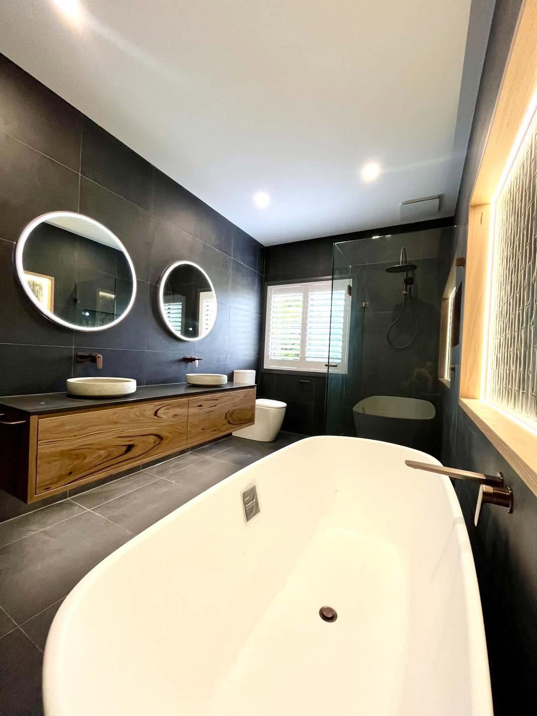Luxury dark ensuite with illuminated round mirrors and timber vanity